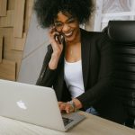 Smiling woman on phone call while working on a laptop in a stylish office.