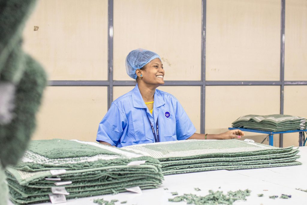 A textile worker in blue uniform smiling while working in a factory.